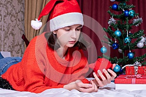 Savings on shopping for Christmas gifts. Sad girl in red christmas hat and sweater pours coins from piggy bank