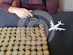 savings for travel, hand of a woman in the calculator, figure of a white airplane and stacked coins of mexican pesos