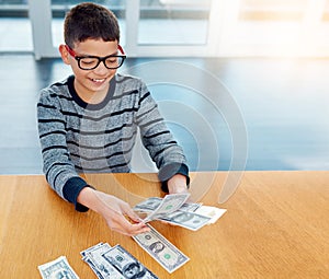 Savings, young child counting money and sitting at desk at his home. Finance or investing, financial management or