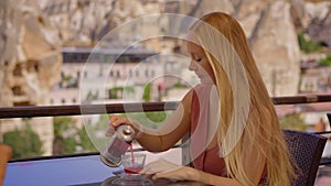 Savor the ambiance of Cappadocia as a young woman enjoys a hot drink on a terrace amidst unique cave houses. The cafe