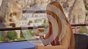 Savor the ambiance of Cappadocia as a young woman enjoys a hot drink on a terrace amidst unique cave houses. The cafe