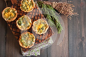 Savory mini quiches tarts on a wooden board. Flaky dough pies.