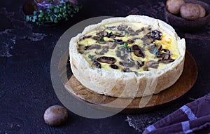 Savory tart, pie or quiche with mushrooms and cheese on wooden plate, dark brown textured background. Homemade savory autumn