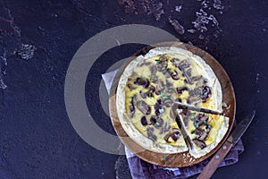 Savory tart, pie or quiche with mushrooms and cheese on wooden plate, dark brown textured background. Homemade savory autumn