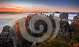 Saxon, Germany - Panoramic view of the Bastei bridge on a sunny autumn sunrise with colorful foliage and heavy fog