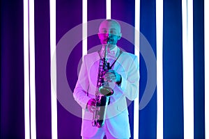 Saxophone player in a white suit against the backdrop of neon lamps with blue backlight. Saxophonist jazzman with sax