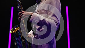 Saxophone player in a white suit performing against the backdrop of neon lamps in a dark studio. Saxophonist jazzman