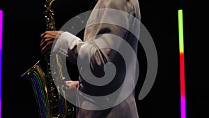 Saxophone player in a white suit performing against the backdrop of neon lamps in a dark studio. Saxophonist jazzman