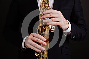 Saxophonist in a black classic suit playing the soprano saxophone on a black background close-up