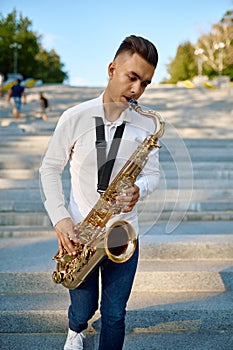 Saxophonist plays the saxophone on stairs in park