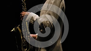 Saxophonist in a white suit performs in the dark. Jazzman with saxophone on black studio background with backlight