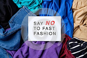 Say NO to fast fashion sign on white paper over heap of female clothes