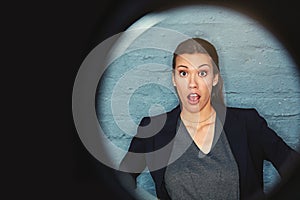 Say whaaat. Portrait of a businesswoman posing against a brick wall with a peephole effect.