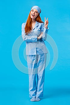 Saying cheeze. Cheerful and cute redhead upbeat girl in glamour pyjama, fancy nightwear having sleepover showing peace