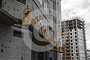 Scaffold elevator hanging on building under construction with gray sky background. house building process
