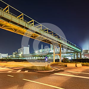 Scaffold with pipeline and Illuminated petrochemical production plant at night.