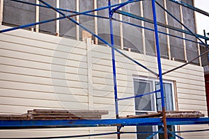 Scaffolding around house with beige siding covering the wall
