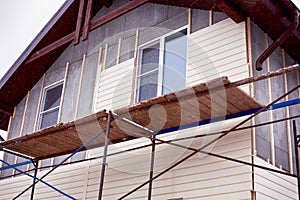 Scaffolding around house with beige siding covering walls.