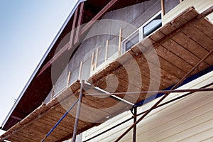 Scaffolding around house with beige siding covering walls. Construction site