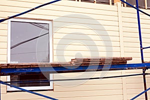 Scaffolding around house near wall with window and beige siding