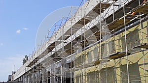 Scaffolding is fixing along the wall of the renovated industrial building in sunny weather, camera is moving