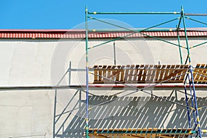 Scaffolding is installed along the wall of the building under construction. Plastering and painting of the facade of the house.