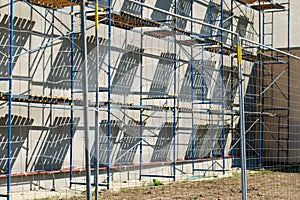 Scaffolding is installed along the wall of the building under construction. Plastering and painting of the facade of the house.