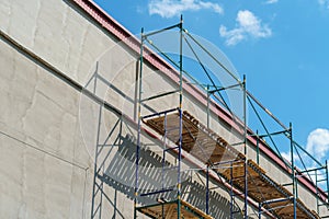 Scaffolding is installed along the wall of the building under construction. Plastering and painting of the facade of the house.