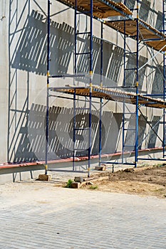 Scaffolding is installed along the wall of the building under construction. Plastering and painting of the facade of the house.