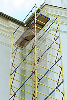 Scaffolding is installed along the wall of the building under construction. Plastering and painting of the facade of the house.