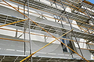 Scaffolding near a house under construction for external plaster works, high apartment building in city, white wall and window, ye