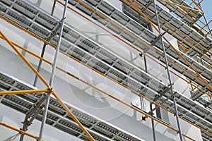 Scaffolding near a new house, building exterior, construction and repair industry, white wall and window, yellow pipe