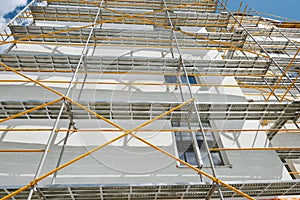 Scaffolding near a new house, building exterior, construction and repair industry, white wall and window, yellow pipe