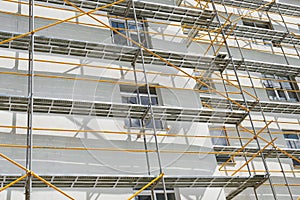 Scaffolding near a new house, building exterior, construction and repair industry, white wall and window, yellow pipe