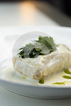 Scalding hot baked cabbage rolls with cream sauce close-up. Restaurant serving of cabbage rolls on a plate with greens