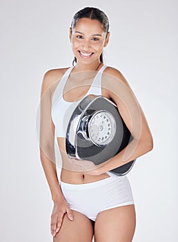 This scale keeps me accountable. Studio portrait of an attractive young woman posing with a weightscale against a grey