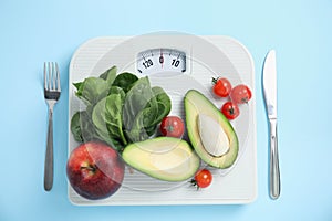 Scales, healthy food and cutlery on light blue background, flat lay