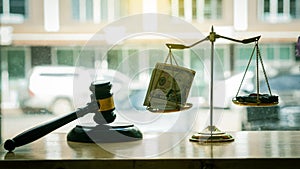 Scales of justice with money and a car lying inside and a lawyer hammer on the table, the background