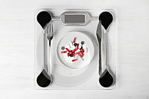 Scales with weight loss pills and cutlery on wooden background