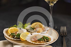 Scallops with lemon on black background with napkin and fork. Baked scallops with caviar in plate against background of blurred