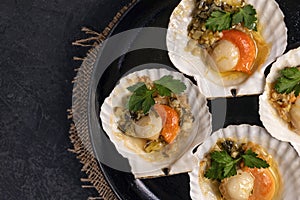 Scallops, lemon, garlic, parsley, butter and salt on black background. Close up baked scallops with caviar and creamy garlic sauce