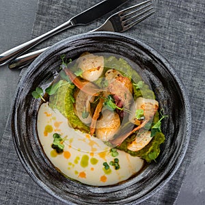 Scallops with mushy peas and Beurre Blanc Sauce. Gray clay plate, spoon, fork on a gray tablecloth photo