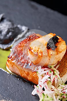 Scallops and ravioli. Seafood, pike perch fish, caviar and black dumplings in a plate on a dark table close-up. Healthy