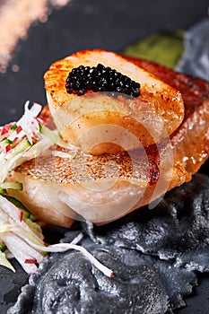 Scallops and ravioli. Seafood, pike perch fish, caviar and black dumplings in a plate on a dark table close-up. Healthy