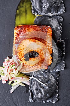 Scallops and ravioli. Seafood, pike perch fish, caviar and black dumplings in a plate on a dark table close-up. Healthy