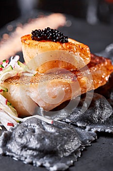Scallops and ravioli. Seafood, pike perch fish, caviar and black dumplings in a plate on a dark table close-up. Healthy