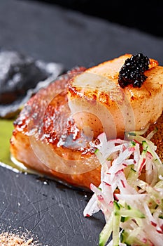 Scallops and ravioli. Seafood, pike perch fish, caviar and black dumplings in a plate on a dark table close-up. Healthy