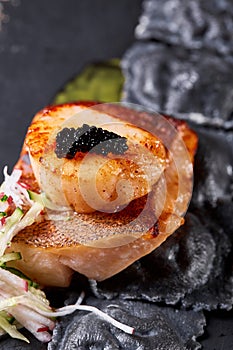 Scallops and ravioli. Seafood, pike perch fish, caviar and black dumplings in a plate on a dark table close-up. Healthy