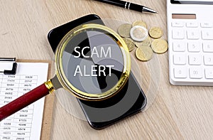 SCAM ALERT text on the magnifier with smartphone, calculator and coins