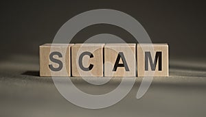 SCAM word made with building wooden blocks on gray